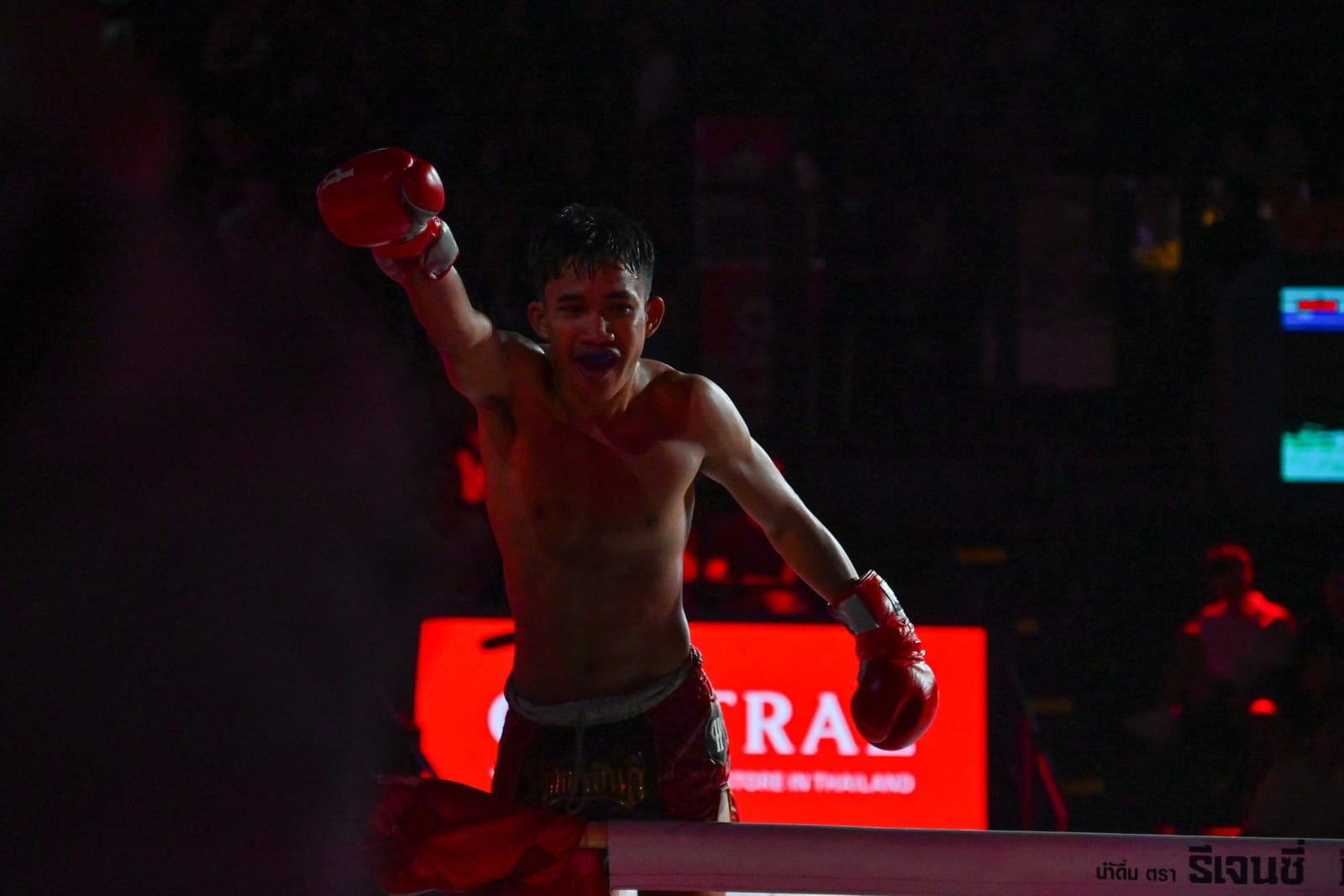 Muay Thai fighter with raised glove lit against a dark arena