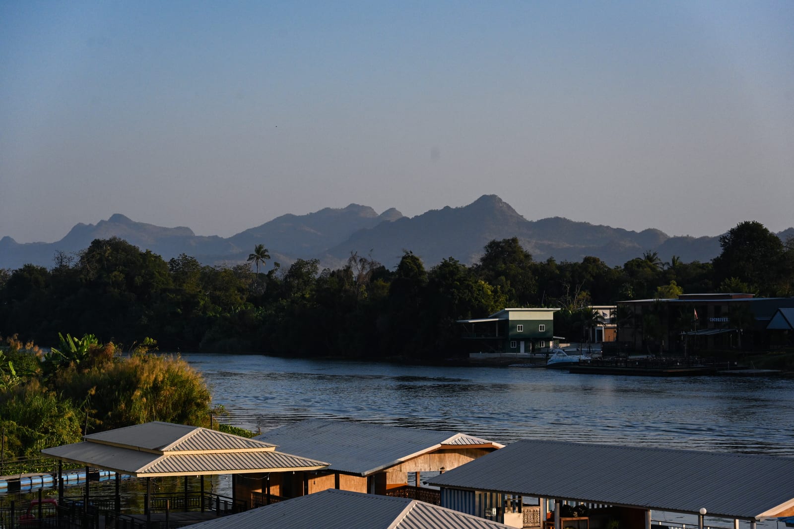 River at dusk with layered mountain ridges and floating houses in the foreground