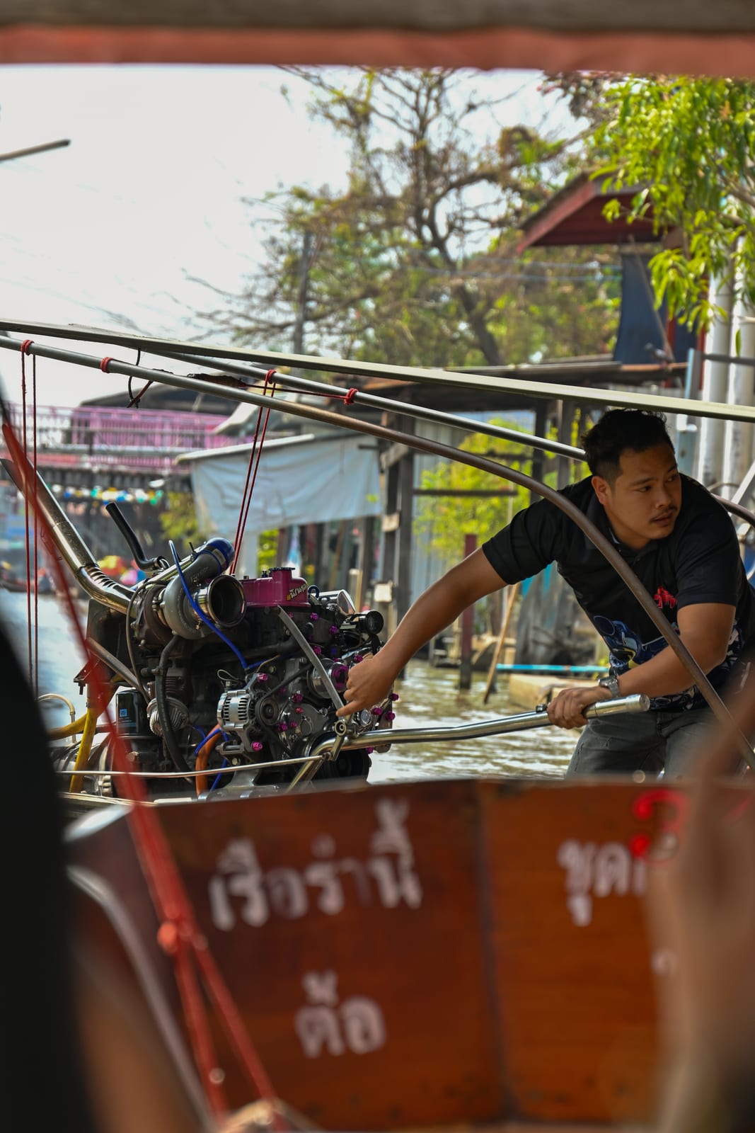Boatman working a longtail engine, framed from inside another boat at the floating market
