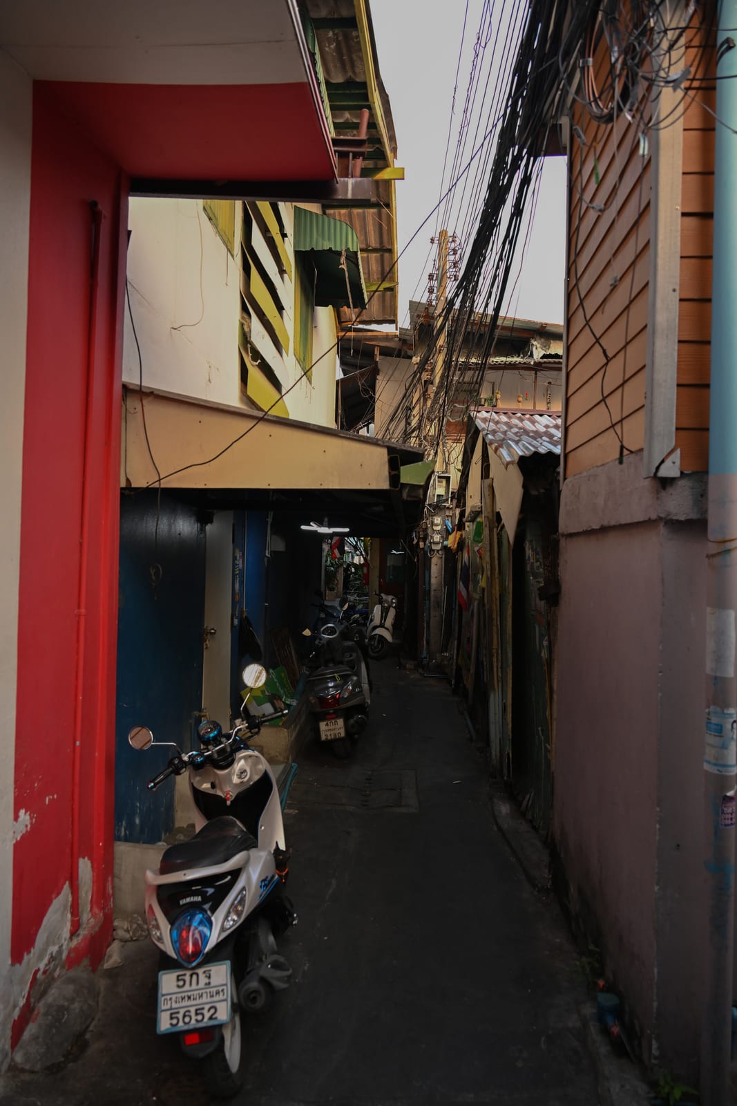 Narrow alley with a red wall, parked scooter and tangled wires
