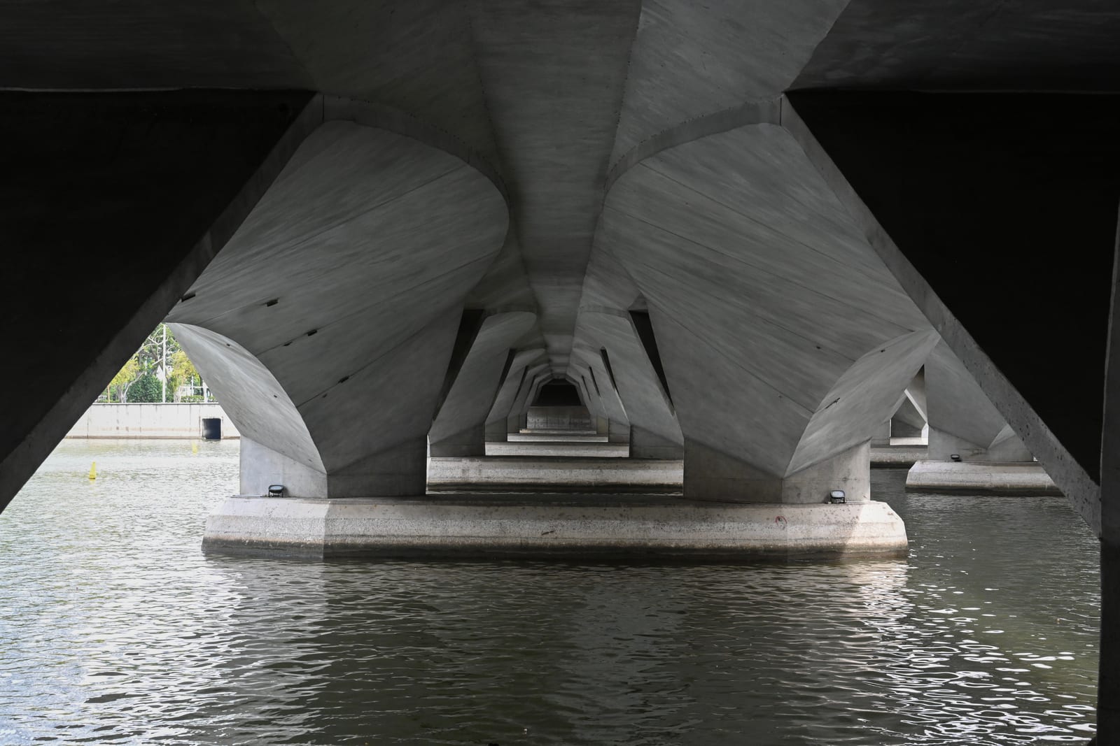 Symmetrical concrete underside of a bridge receding over water in near monochrome
