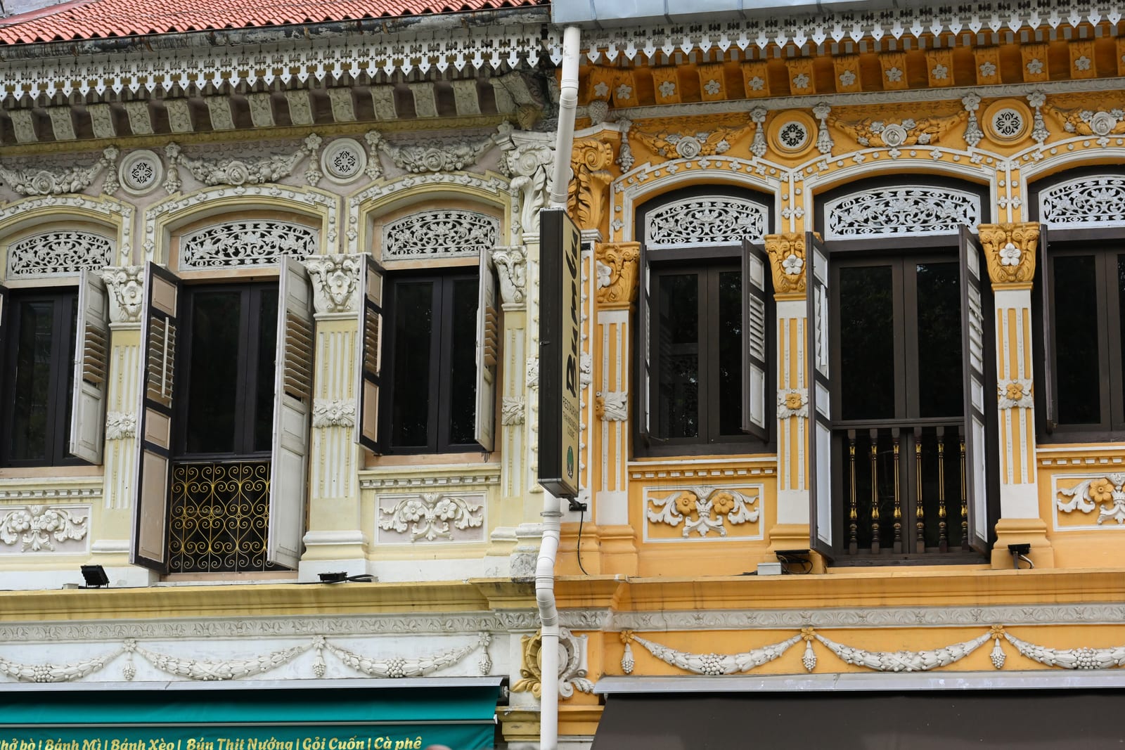 Ornate yellow and cream Peranakan shophouse facade with shuttered windows
