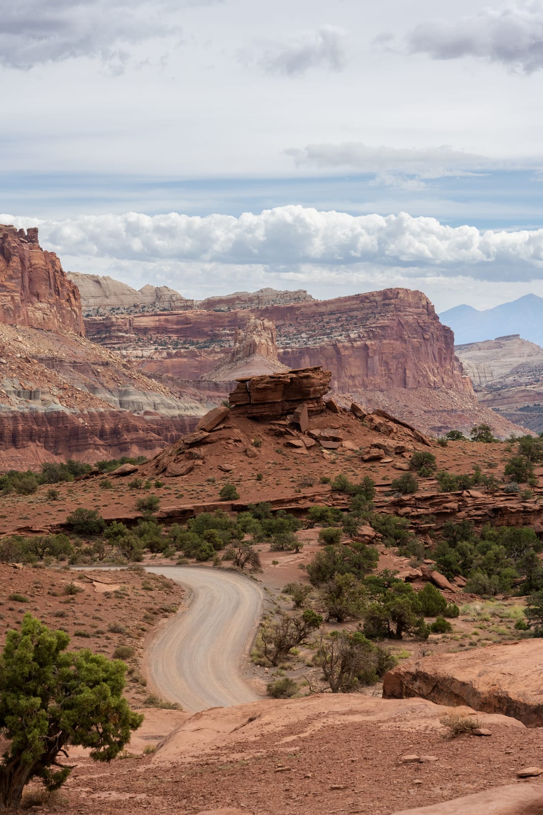 Dirt road winding toward red cliffs and buttes under a cloudy sky in Capitol Reef