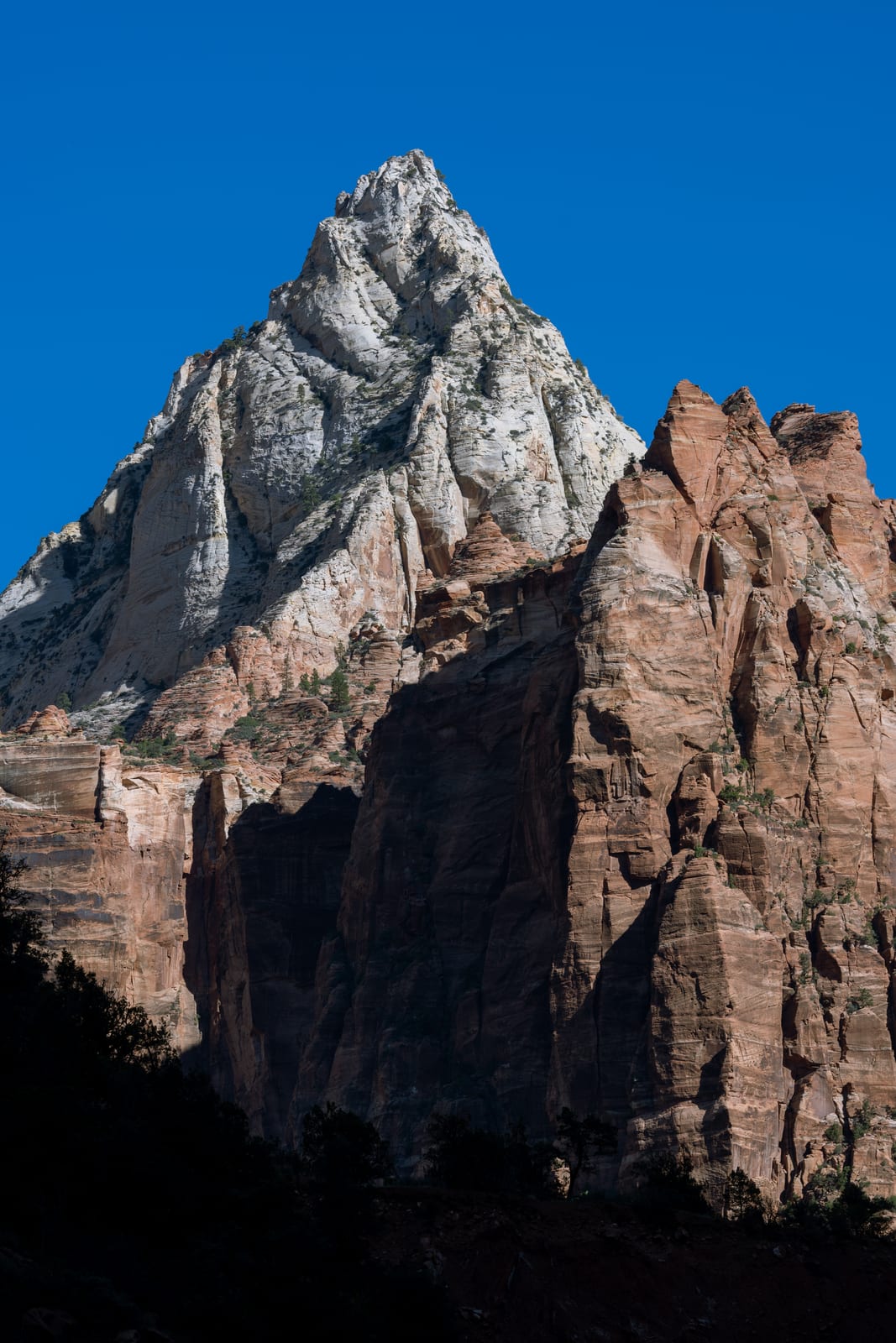 White-capped sandstone peak above red cliffs against deep blue sky, dark foreground
